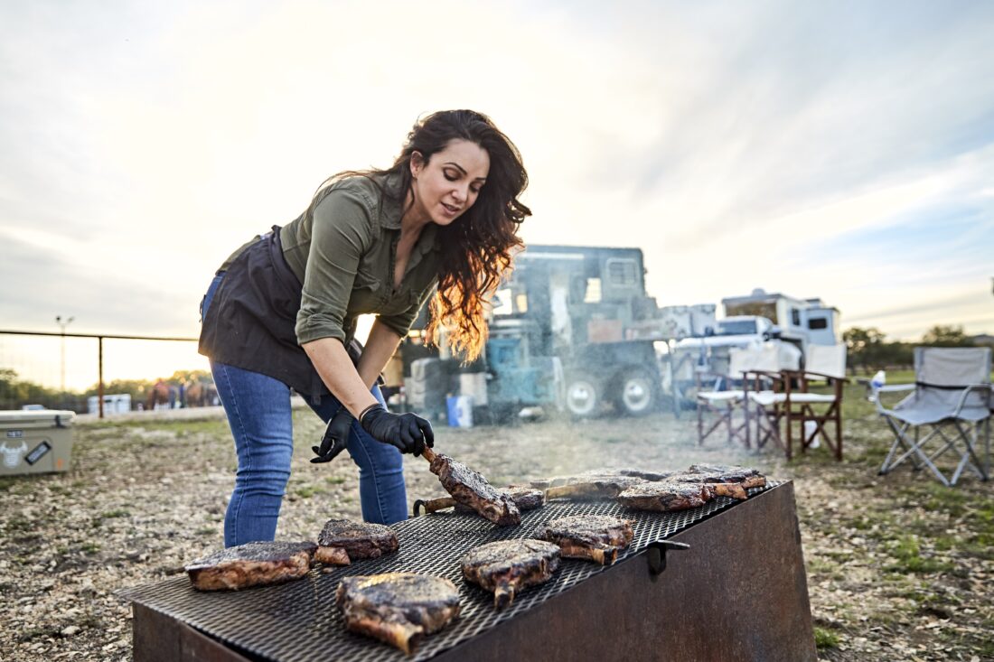 A woman turning steaks on a grill