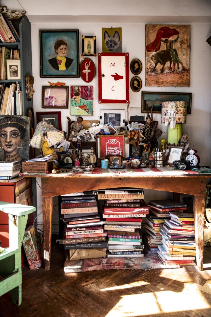 A desk covered with books and a wall behind it covered with artwork