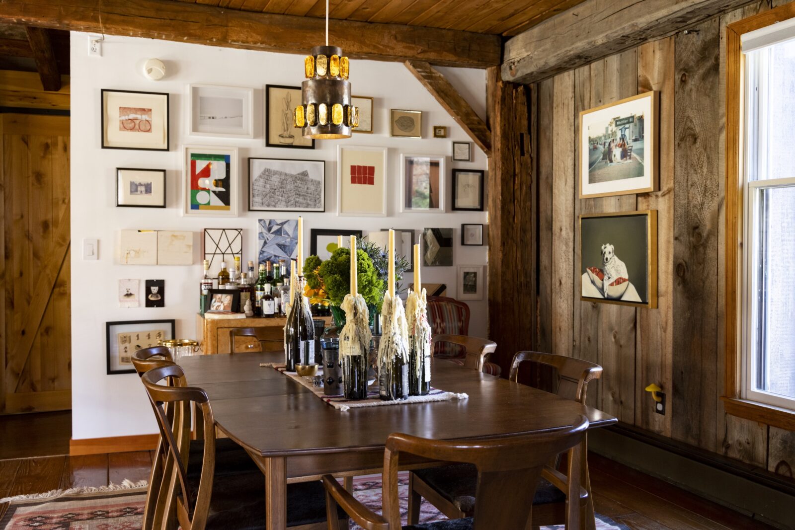 Drippy candles set on a dining table in a kitchen. The wall is covered with artwork