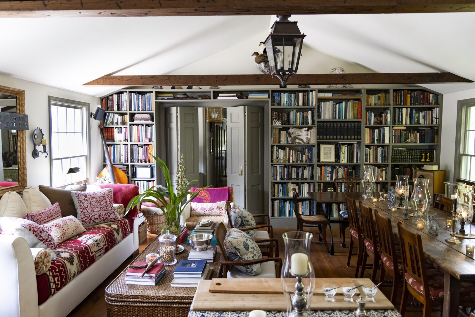 A layered, maximalist living room with stacks of books and colorful pillows