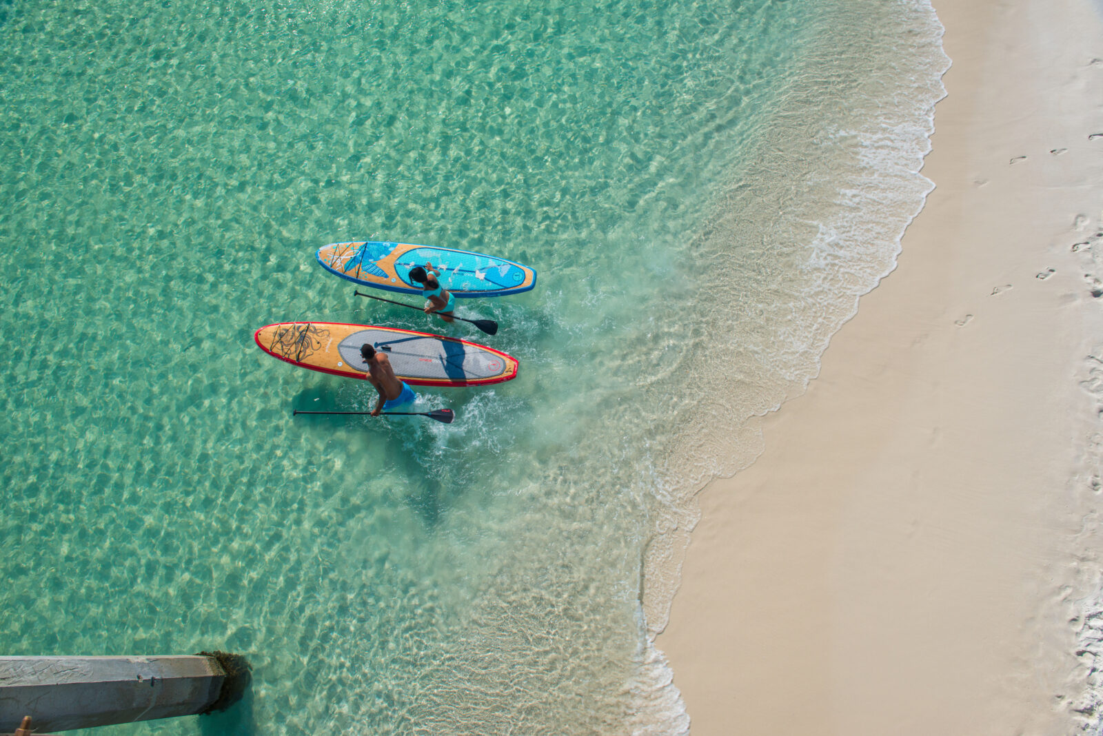 Two people paddle board on a clear water beach