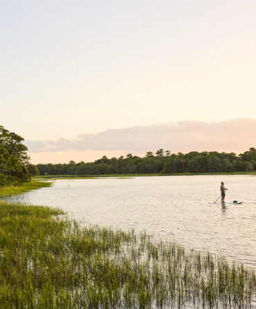 two people paddleboarding in a marsh at sunset