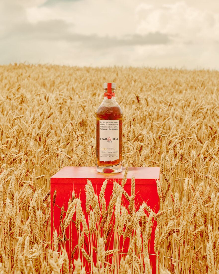 A bottle of whiskey in a wheat field on a red stand