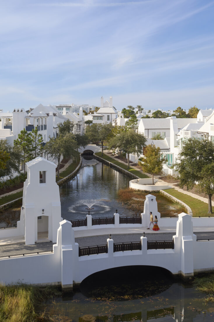 People walk over a small walking bridge in a white-painted villa