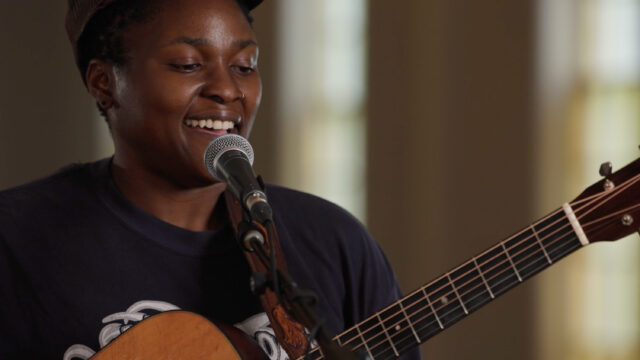 A woman holding a guitar at a microphone