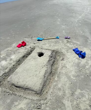 A cornhole hole made in the sand