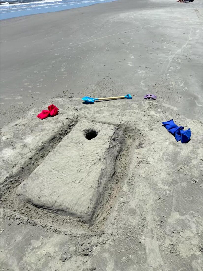 A cornhole hole made in the sand