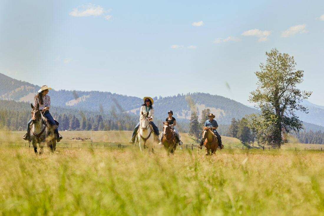 People ride horses in a field with mountains