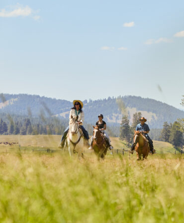 People ride horses in a field with mountains