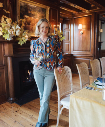 A woman in a patterned blouse stands in a wood-paneled dining room