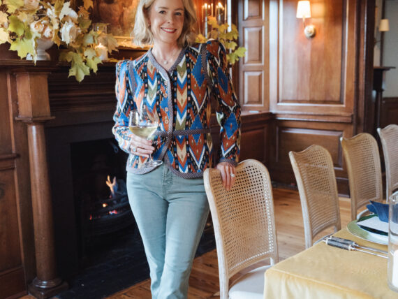 A woman in a patterned blouse stands in a wood-paneled dining room