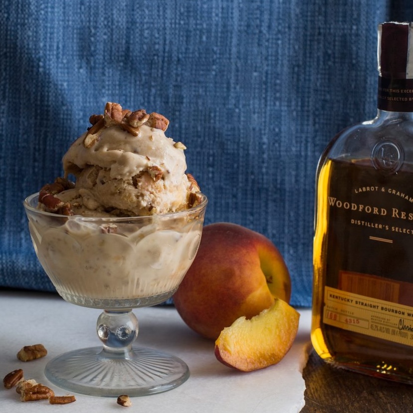 a scoop of bourbon butter peach ice cream in a glass bowl with a peach and bourbon