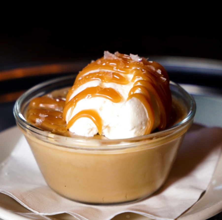 a bowl of butterscotch pudding with whipped cream, drizzled caramel and sea salt