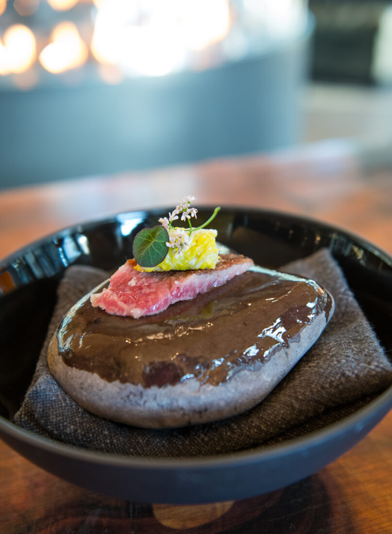 an amuse-bouche of Hokkaido beef and ginger displayed on a river stone