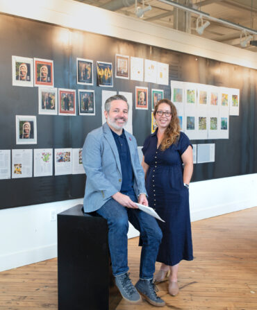 A man and woman stand in front of a wall with pages of a magazine