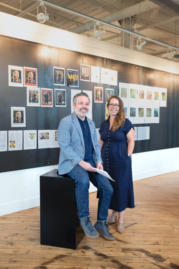 A man and woman stand in front of a wall with pages of a magazine
