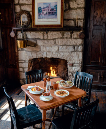 A table with four chairs with dishes next to a stone fireplace