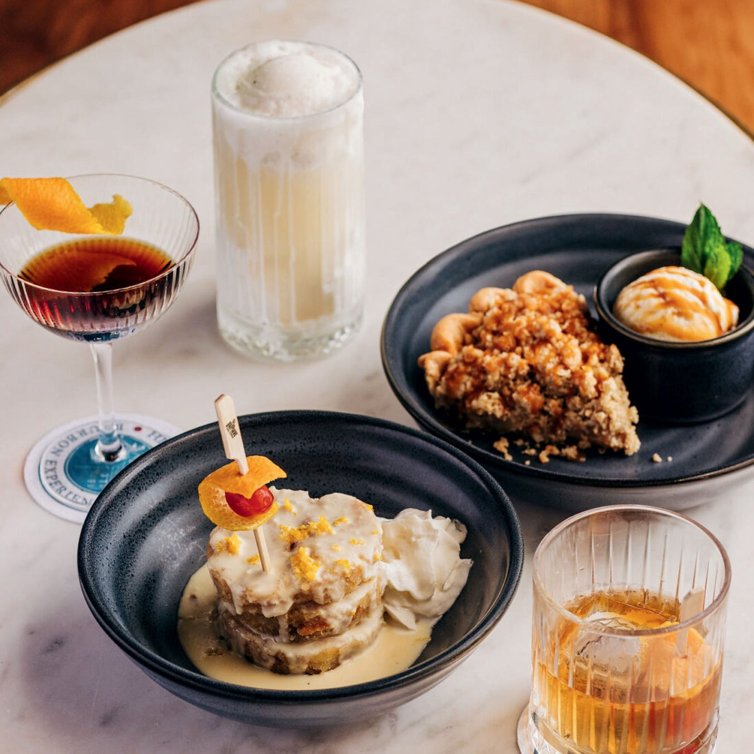 Two plates of food with three drinks surrounding them on a table