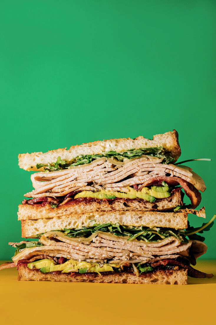 A stacked sandwich with avocado and sliced meat