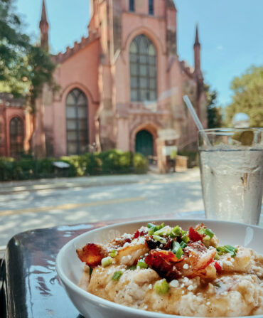 A plate of food and a drink next on a table across the street from a pink church