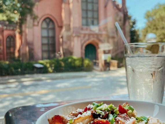 A plate of food and a drink next on a table across the street from a pink church