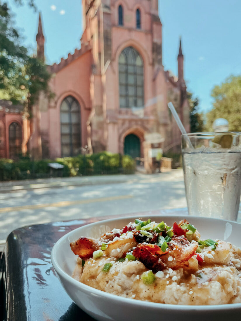 A plate of food and a drink next on a table across the street from a pink church