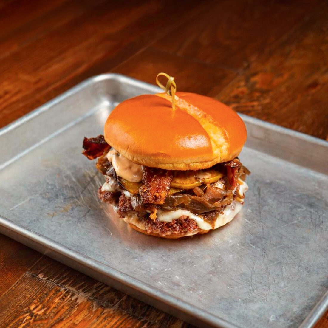 A burger with bacon and sauce on a silver tray