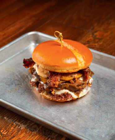 A burger with bacon and sauce on a silver tray