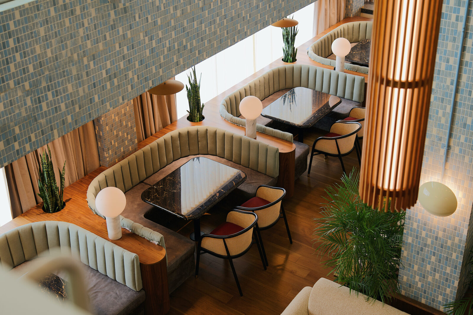 A booth with blue tiles and curved wood and green cushioned sofas