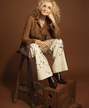 A portrait of a woman sitting on a stool against a brown background