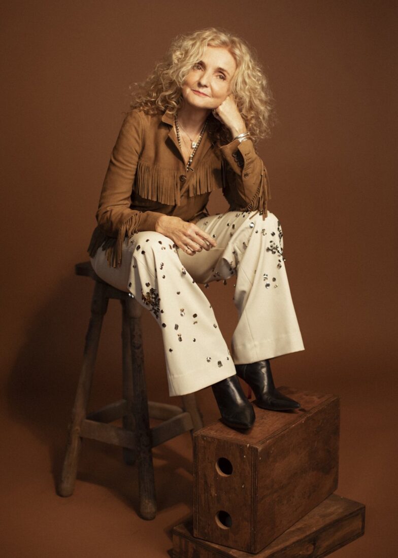 A portrait of a woman sitting on a stool against a brown background