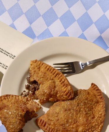 two plates of food on a blue and white checkered tablecloth with fries, ketchup, hot sauce and a cup of coffee