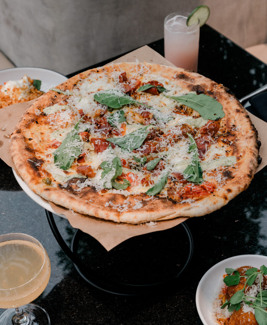 A pizza on a stand surrounded by cocktails