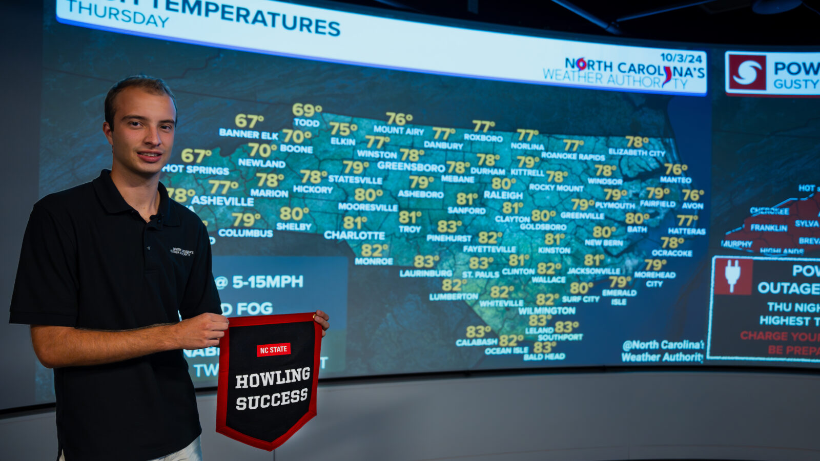 A man poses with a banner in front of a weather screen