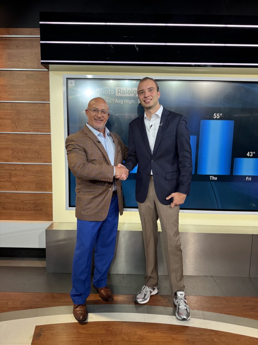 Two men shake hands in a weather channel room