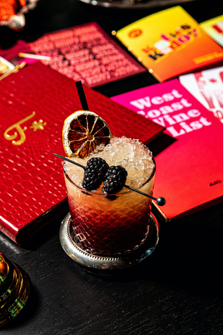 A blackberry cocktail with pink cards in the background