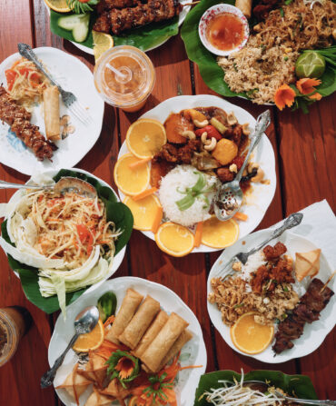 Pork skewers, egg rolls, pad thai, cashew chicken, and other dishes on a table