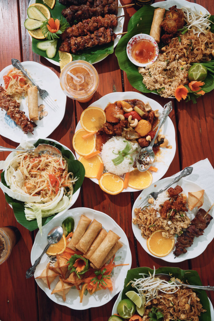 Pork skewers, egg rolls, pad thai, cashew chicken, and other dishes on a table