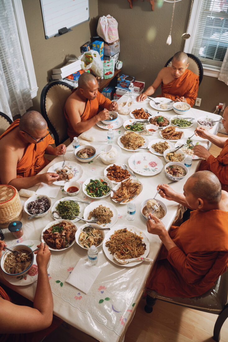 Monks in orange robes sit at a long table with thai food