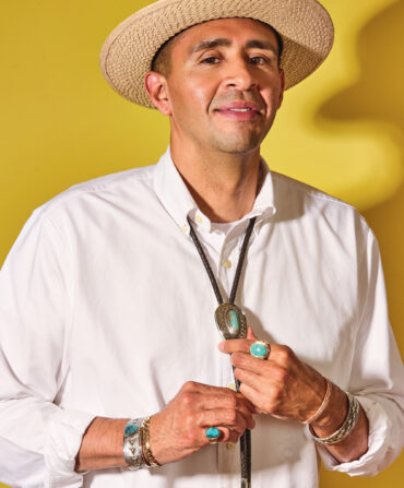 A portrait of a man with stunning jewelry. He stands against a bright yellow background