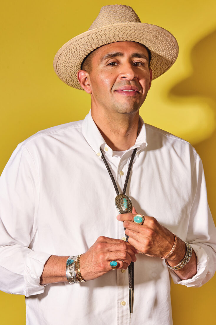 A portrait of a man with stunning jewelry. He stands against a bright yellow background