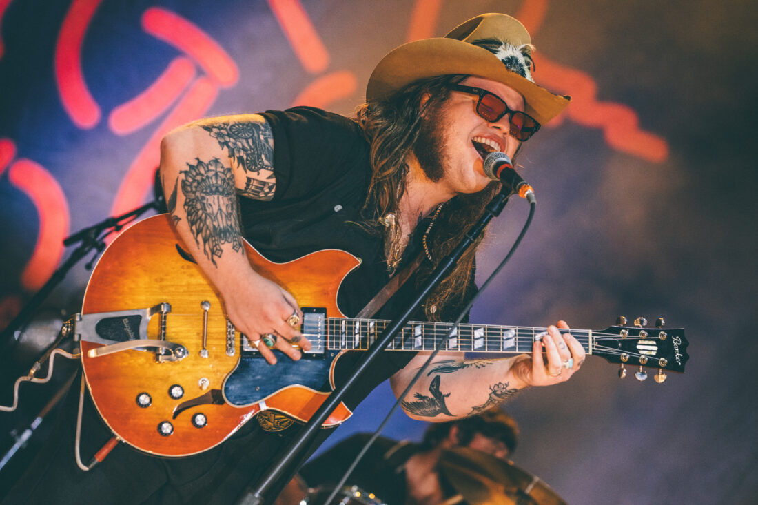 A portrait of a man singing on a stage holding a guitar