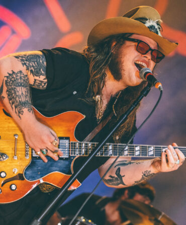 A portrait of a man singing on a stage holding a guitar