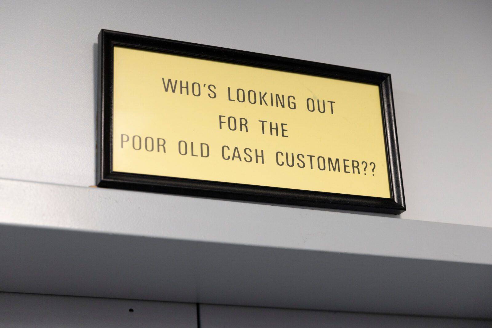 “Who’s Looking Out for the Poor Old Cash Customer??” on a metal plaque on a wall