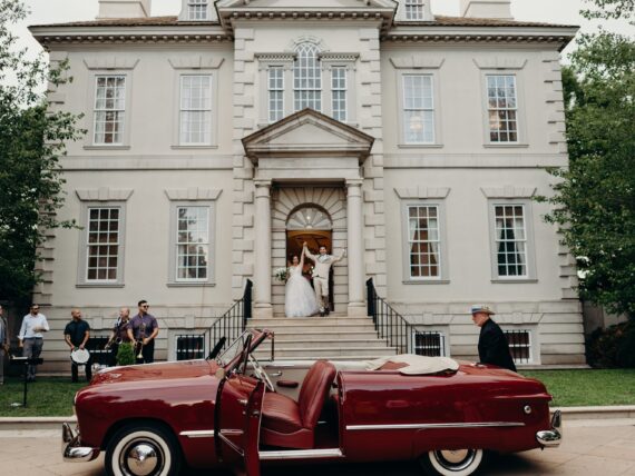 a bride and groom exit a church in front of a custom Ford convertible