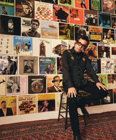A man sits on a chair by a wall of records