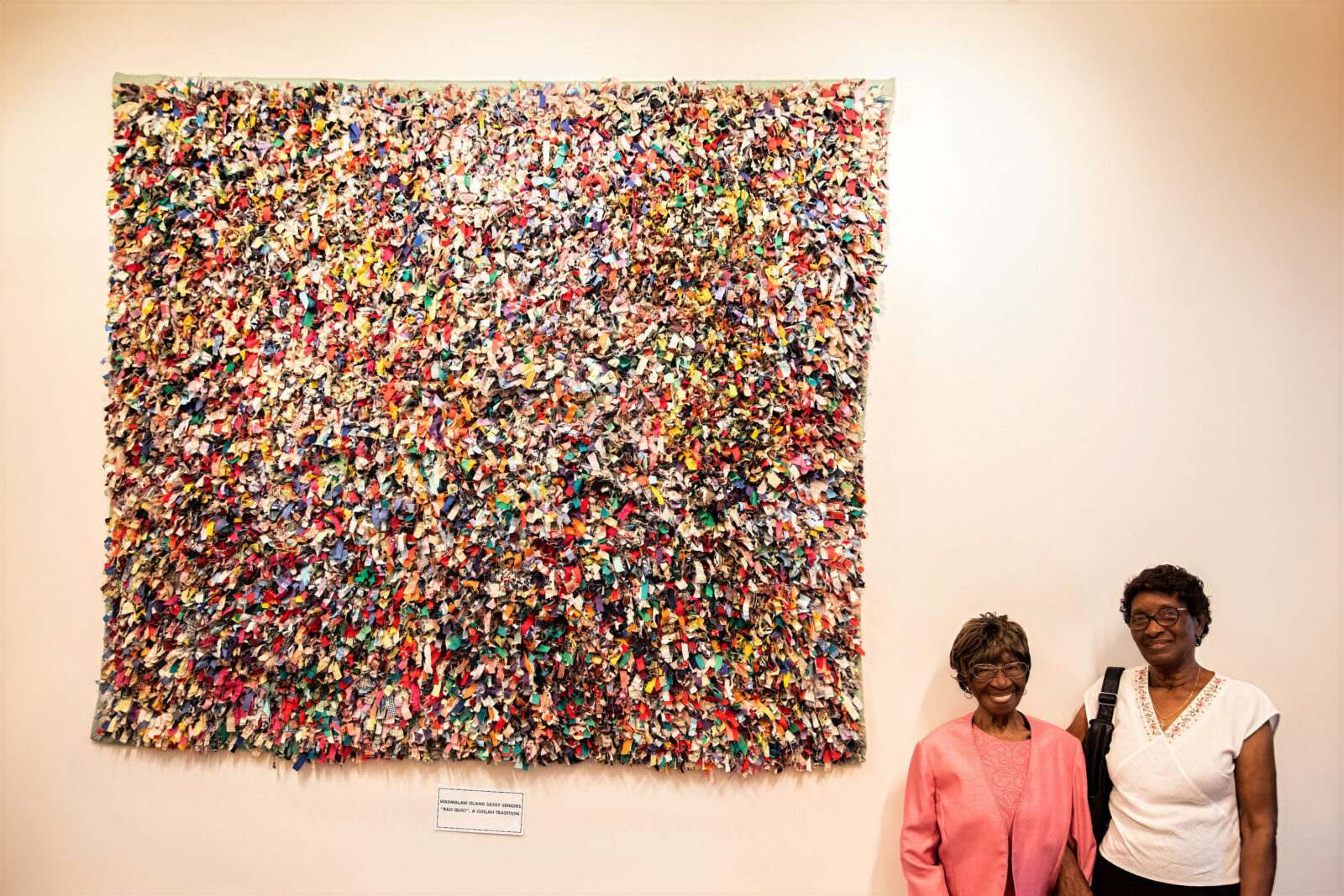 Two women stand by a rag quilt
