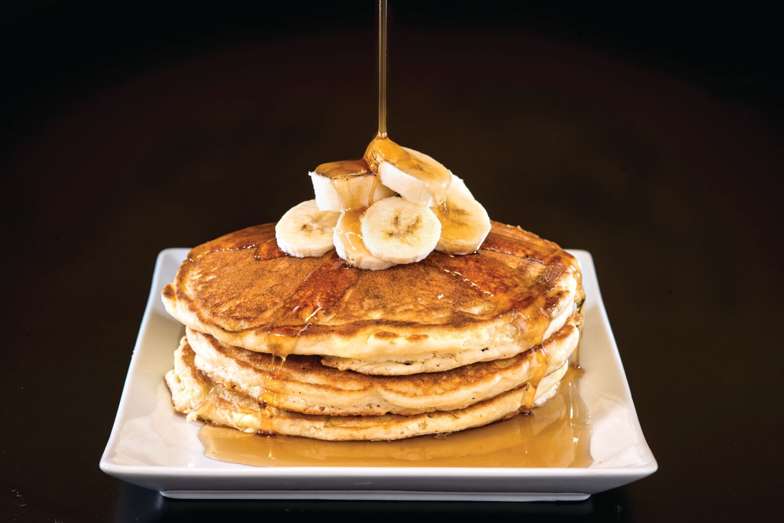 syrup being poured over banana pancakes