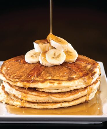 syrup being poured over banana pancakes