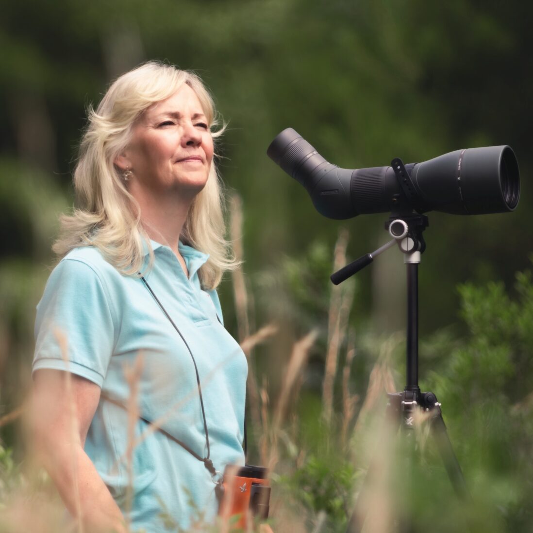 A woman stands in a field with a scope